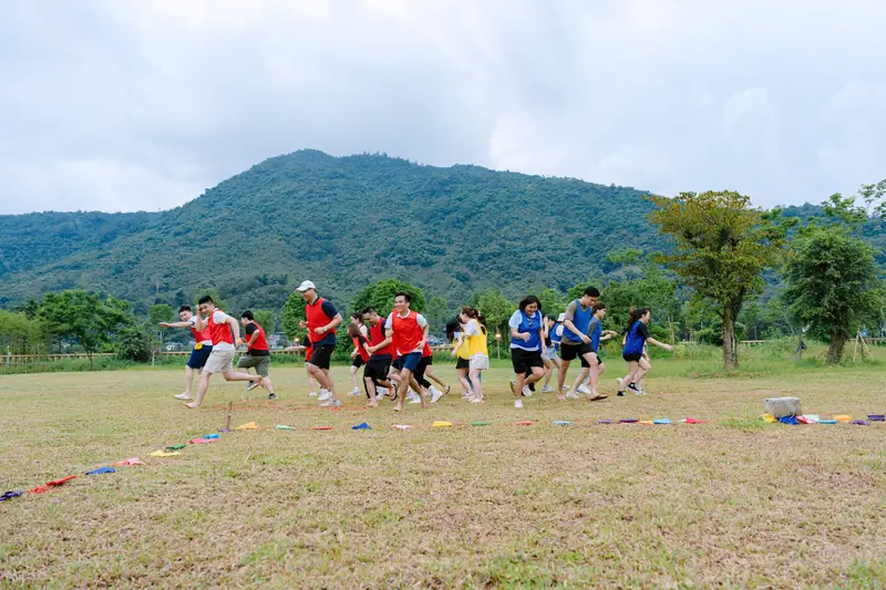 Đoàn khách chơi trò chơi team building trên sân cỏ rộng, phía sau là núi